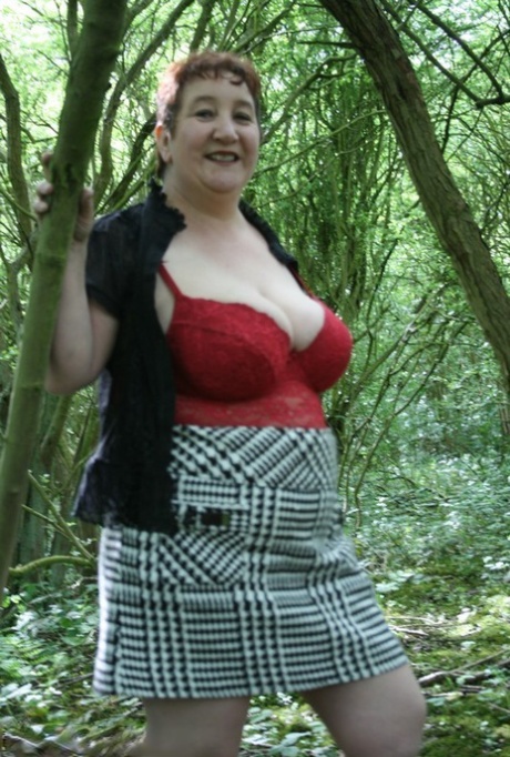 Mature lady Kinky Carol shows her huge tits and butt amid undergrowth