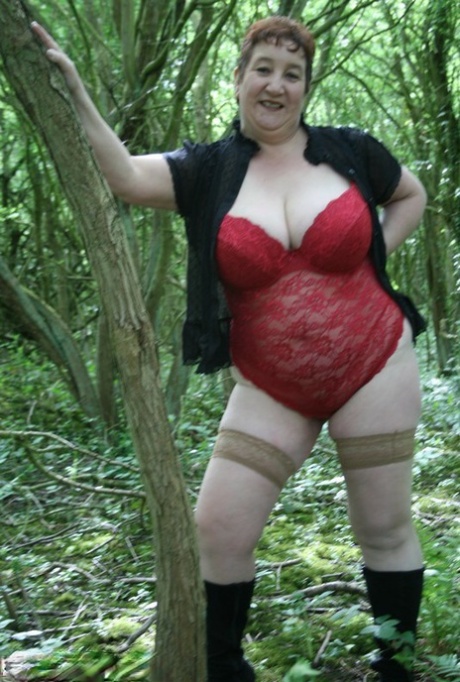 Mature lady Kinky Carol shows her huge tits and butt amid undergrowth