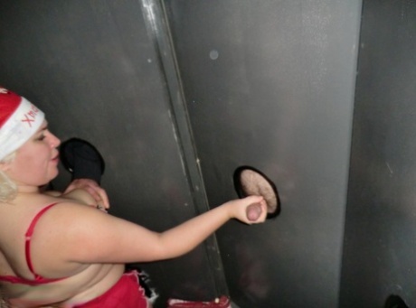 BBW Barby, who is blonde, engages in sexual activity by giving a blowjob at gloryholes.