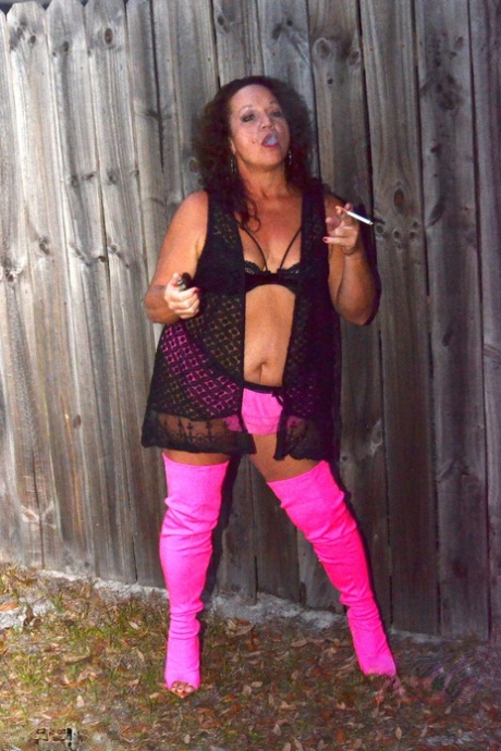 Smoking by the fence is a common sight for Debbie Delicious, an elderly woman who is not skilled in smoking, while wearing pink thigh high boots.