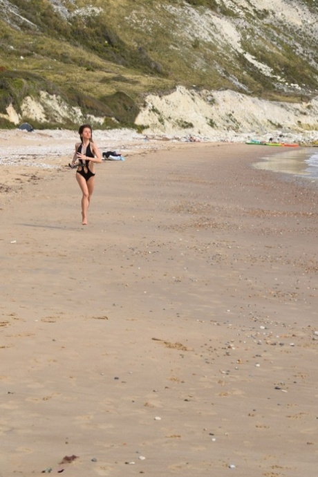 Short women pose in a bathing suit on a deserted beach.