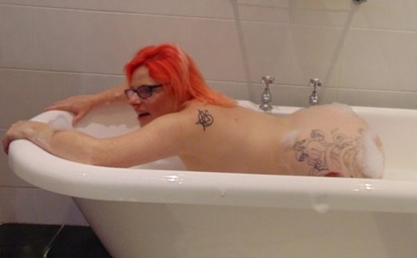 A bubble bath is enjoyed by Mollie Foxxx, the amateur with a tattoo on her face, while she wears glasses.