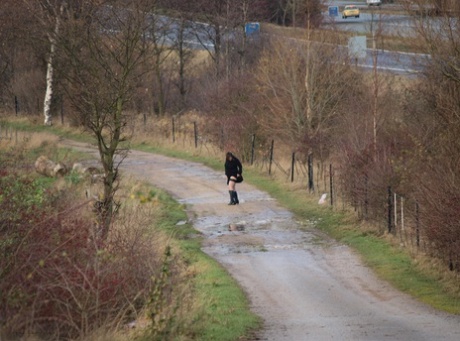 In her black boots, Roxy exposes herself while walking along a path as an overweight woman.