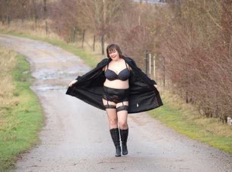 The overweight Roxy exposes herself while walking in black boots on a path.