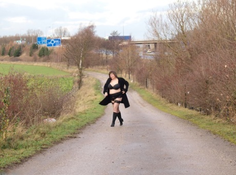 In black boots, Roxy exposes herself while walking along a path as an obese woman.