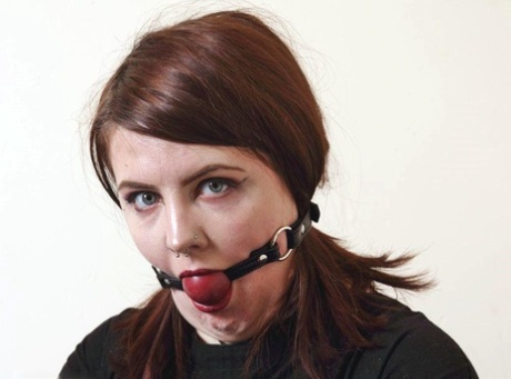 With her tattooed red hair and straps tied around her body, Luna La Roux exhibits a ball gag.