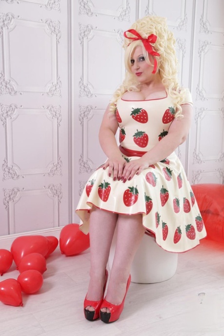 Thick blonde Avengelique models a latex dress with hosiery and red heels.
