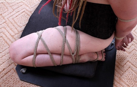 A white girl is tied up with rope in a corset while being silenced with duct tape.