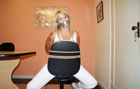 A desk chair is secured to a blonde amateur, and the individual is silenced by using duct tape.