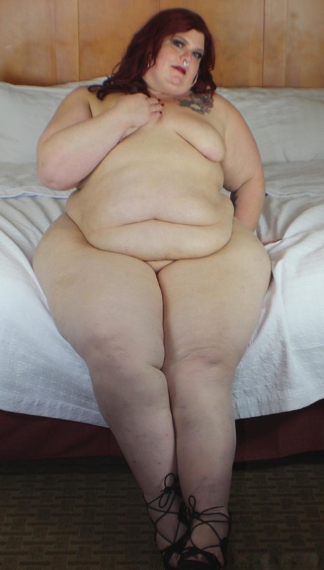 With her massive buttocks visible, Redhead SSBBW Nikki Cakes poses on a bed with her face down.