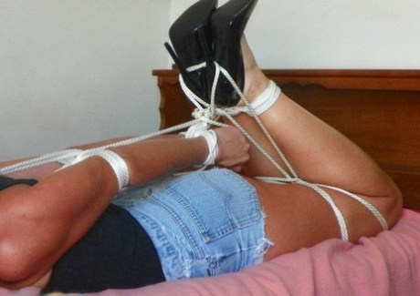 A female garment is tying up on a single bed while being tied up with rope.