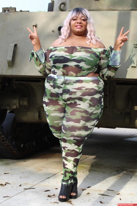 Black woman Carmelotto Rush, who is obese, displays her thong-clad buttocks on the opposite side of a tank.