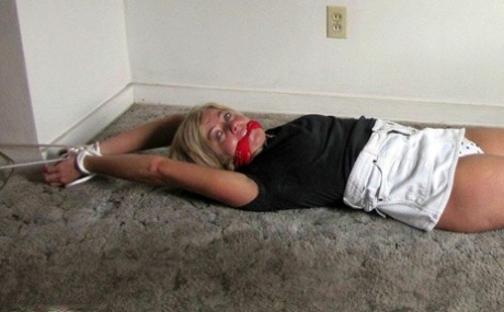 A blonde who is gagged with her ankles and wrists tied down with rope while she.