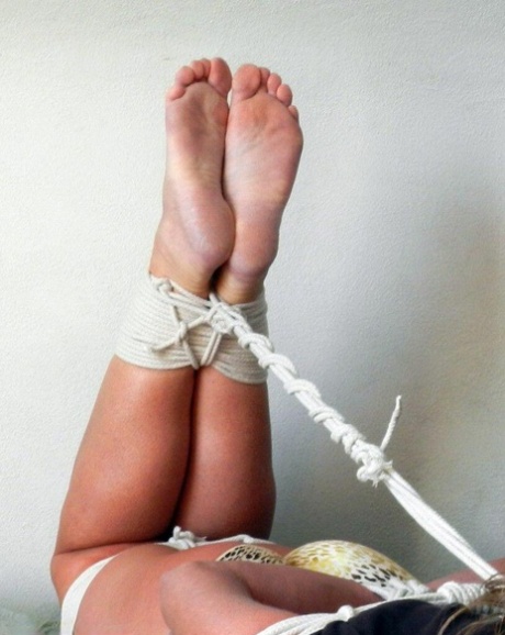 Barefoot blonde is tied up with rope and heavily splayed on a bed.