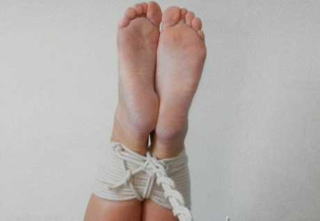 On a bed, blonde hair on the feet is tightly bound with rope and heavily gagged.