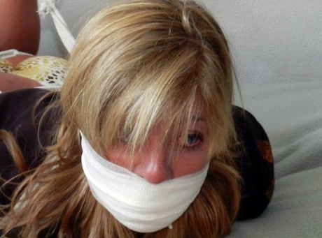 The blonde's feet are tightly bound with rope on a bed, leaving them heavily gagged.