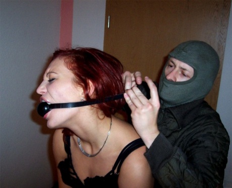 Black bearded man: Redhead Lilu Natilova is tied up and gagged by a man wearing a mask on.