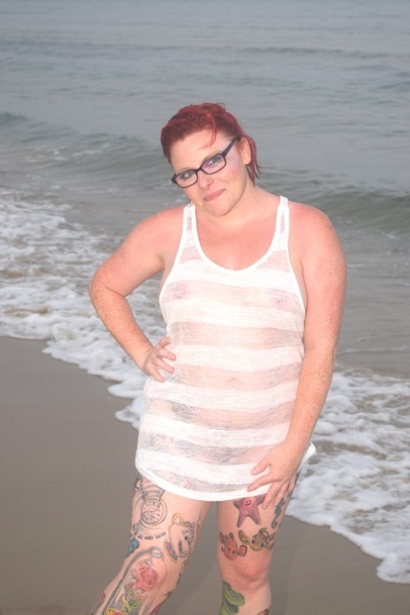 Before exposing herself, the tattooed redhead wades into the ocean.