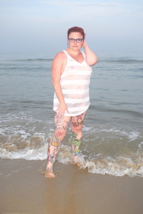 Redhead tattooed woman wades into the ocean before exposing herself.
