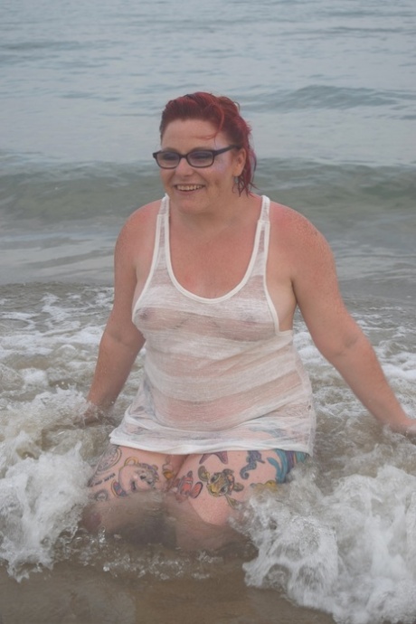 Prior to exposing herself, the tattooed redhead wades into the ocean.