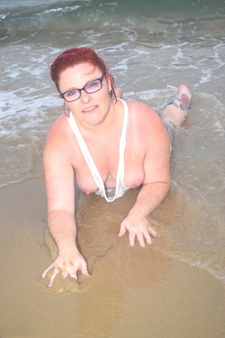 Exposed woman with tattooed red hair wades into the sea before exposing herself.