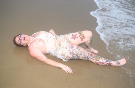 The redhead, with tattooed hands, dives into the ocean before exposing herself.