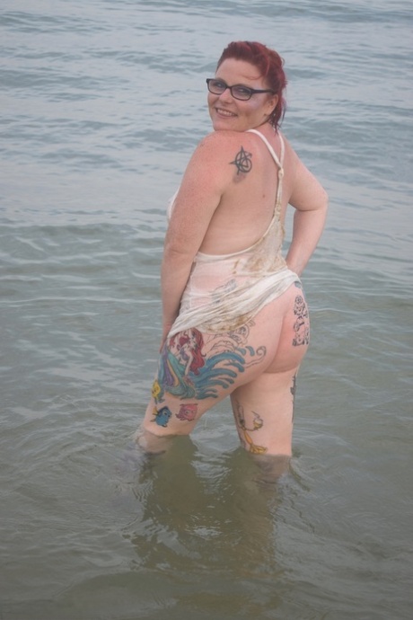 Before exposing herself, the tattooed redhead wades into the ocean.