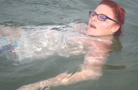 Redhead with tattooed features float into the sea before exposes herself.