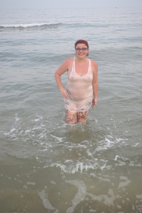 A tattooed individual with red hair ventures into the sea before exposing herself.