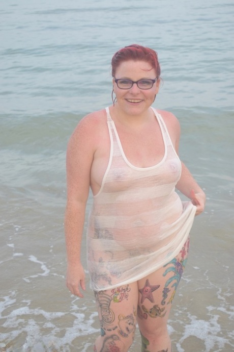 A tattooed individual sporting red hair takes a swim in the ocean before exposing herself.