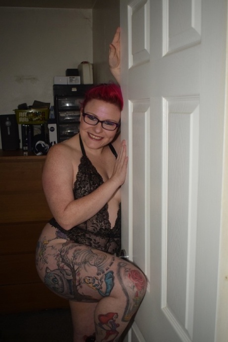 Mollie Foxxx, an amateur with tattoos, models herself in black lingerie while wearing glasses.