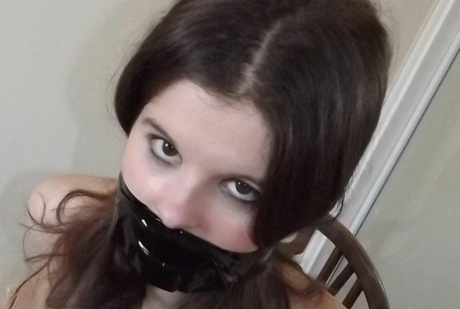 Clothed girl Tamara looks in a mirror while gagged and restrained to a chair