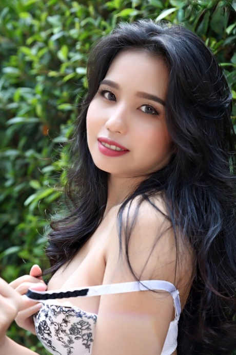 Surrounded by a hedge in the garden, Norah, an attractive Asian girl, goes completely naked during her pose.