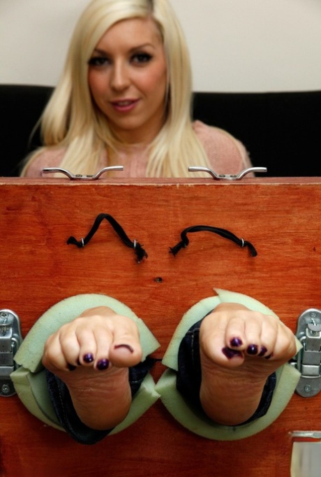 Blonde chick Alex Adams wiggles her toes while her feet are in stocks