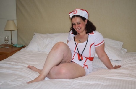 The overweight nurse removes her attire and models herself in black panties on a bed.