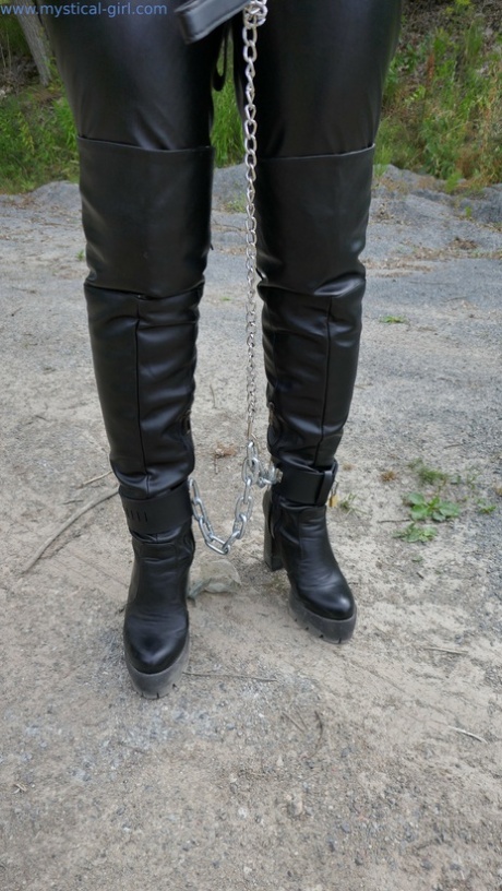 A woman with a collar is restrained with cuffs and chains while wearing leather.