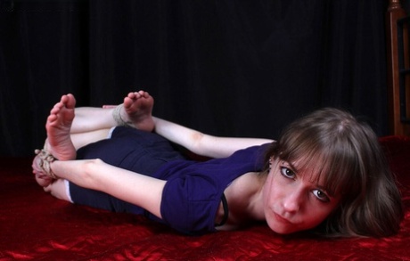 Wearing her clothes, Agnes finds herself lying face down with her wrists tied around her ankles.