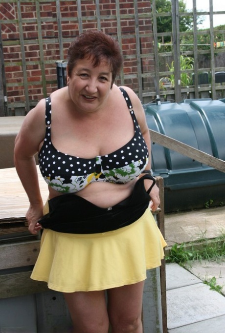 Kinky Carol, an elderly and thick woman, models a bikini on patio stones.