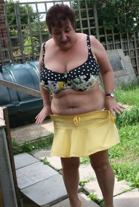 On patio stones, Kinky Carol, a heavier woman of considerable size, models a bikini on the backside.