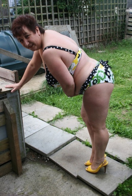 A bikini is worn by a taller woman, Kinky Carol, on patio stones.