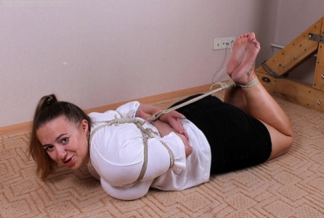 The Caucasian female, Charlotte, is seen wearing a blouse and miniskirt, while also being hogtied.