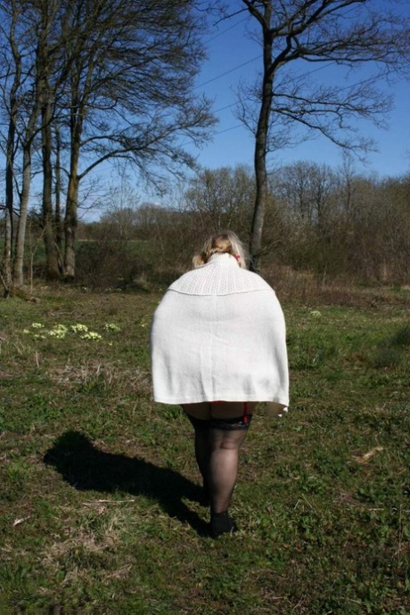 In a field, Lexie Cummings, an obese British blonde, exposes her stomach and large buttocks.