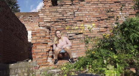 Белая девушка прячется за старым зданием, чтобы срочно помочиться