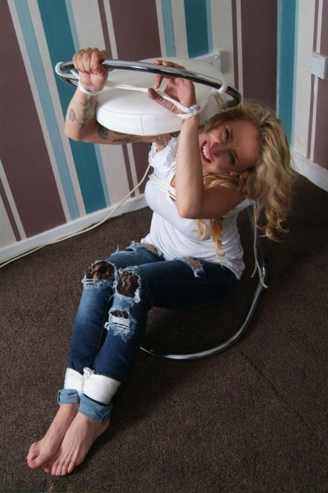 While being restrained with rope bindings, Katie C, who is fully clothed in blonde, struggles to move forward.