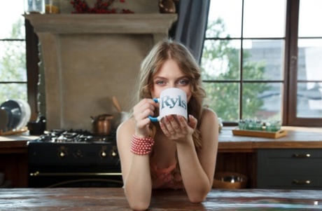 Симпатичная молодая девушка Сия раздевается на кухонном столе за чашкой кофе