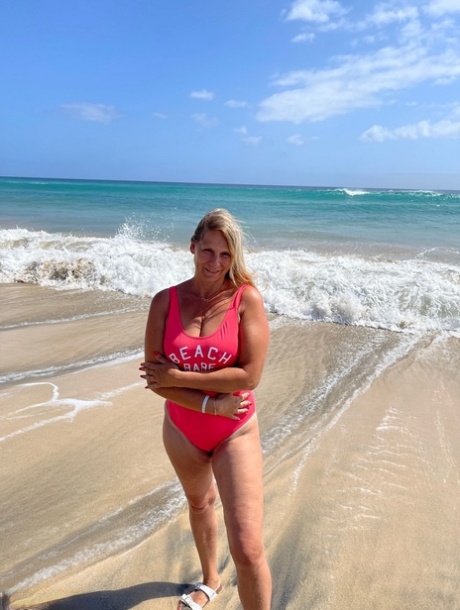 A naked Sweet Susi, who is middle-aged blonde, walks on a sandy beach.