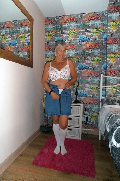 Granny Savana, with her silver hair on her legs and arms in the bedroom, bares white socks for her knees.