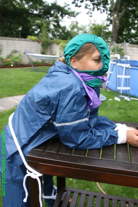 A white woman is tying herself to a table in a yard, draped in panties over her face.