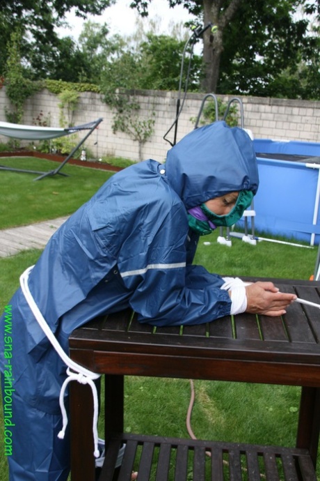 A white lady sits with her pants down on her face in a backyard and is tied to a table in the yard.