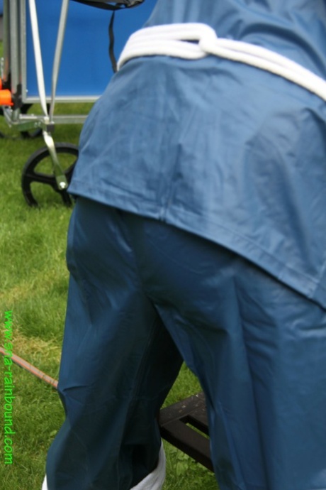 Dressed in panties, a white woman is tied to a table and hiding behind the cover of grass in a yard.